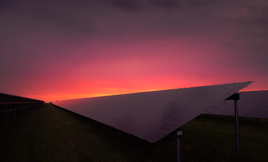 Solar panels in a field at sunset with a vibrant pink and orange sky