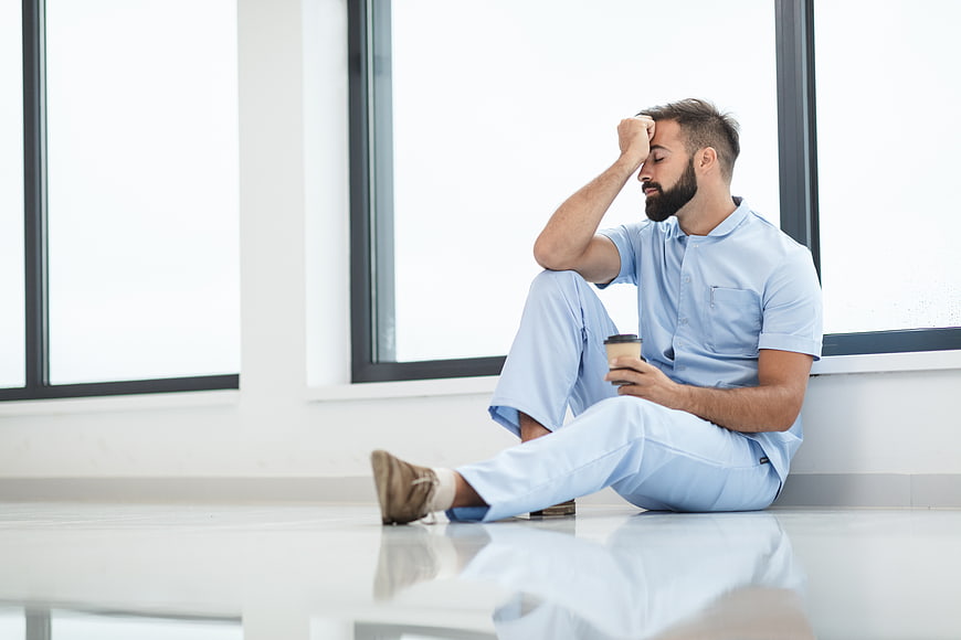 Exhausted male nurse sitting on hospital floor with coffee