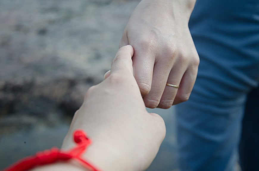 Close-up of couple holding hands with red bracelet and gold ring