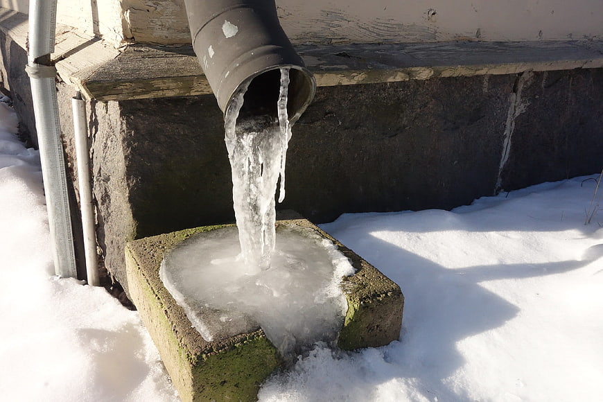 Frozen drainpipe with icicles and ice in winter snow