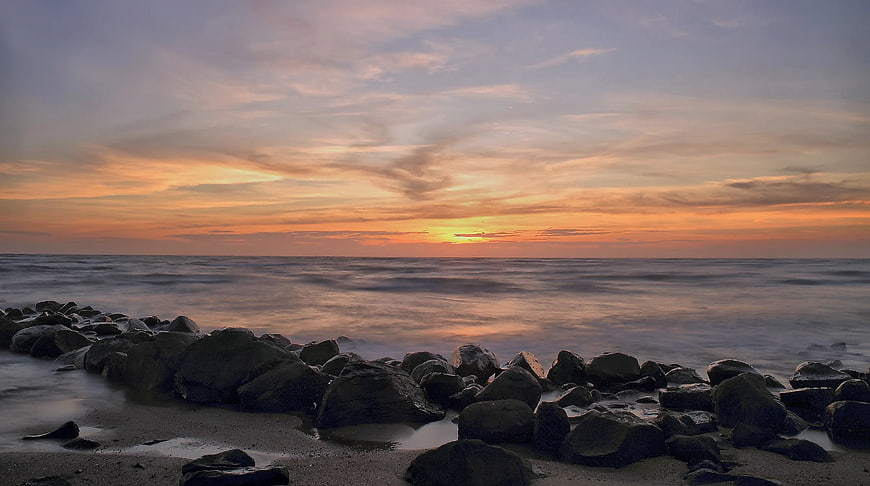Serene Sunset Over Rocky Beach with Smooth Ocean Waves