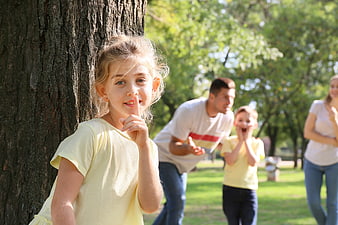 Cute Girl Shushing While Family Plays Hide and Seek in Park