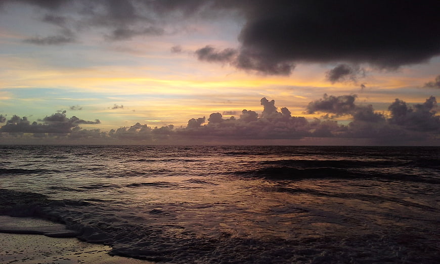 Dramatic Sunset Over Ocean with Dark Clouds and Golden Sky