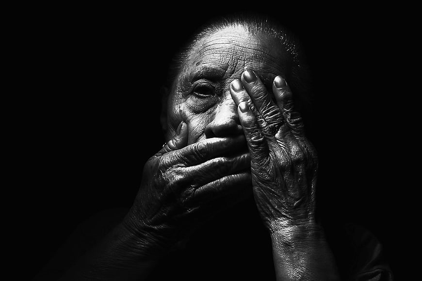 Dramatic black and white portrait of elderly woman covering face