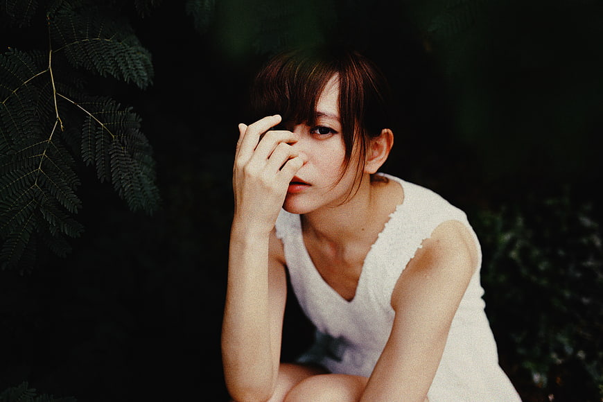 Melancholic woman in white dress touching face outdoors