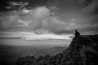 Silhouette of Man Sitting on Rocky Cliff Edge Overlooking Valley