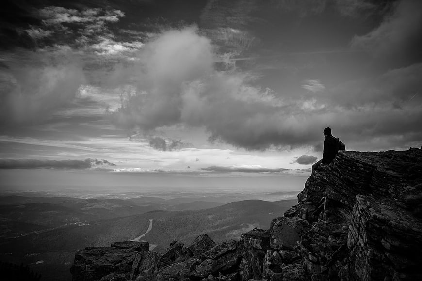 Silhouette of Man Sitting on Rocky Cliff Edge Overlooking Valley