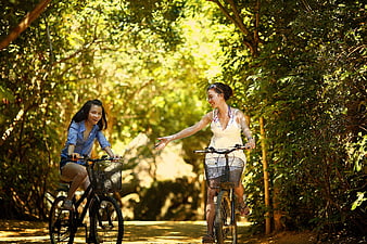 Two Happy Women Cycling on a Sunny Forest Path