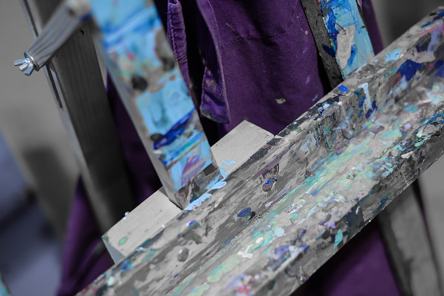 Close-up of paint-splattered wooden easel with purple cloth