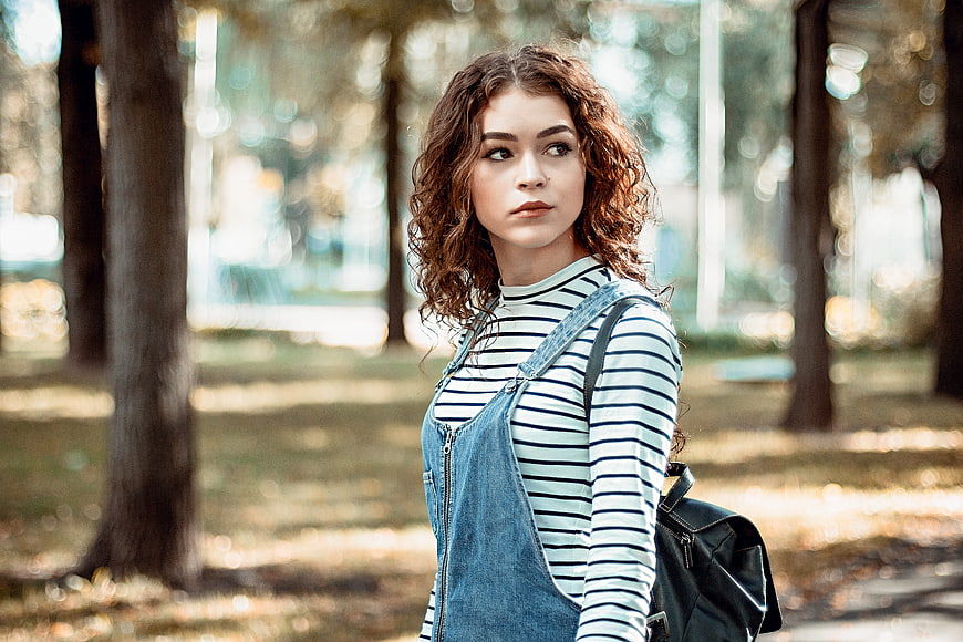 Young woman with curly hair in denim overalls outdoors