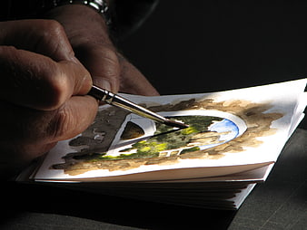 Close-up of artist hand painting watercolor landscape in sketchbook