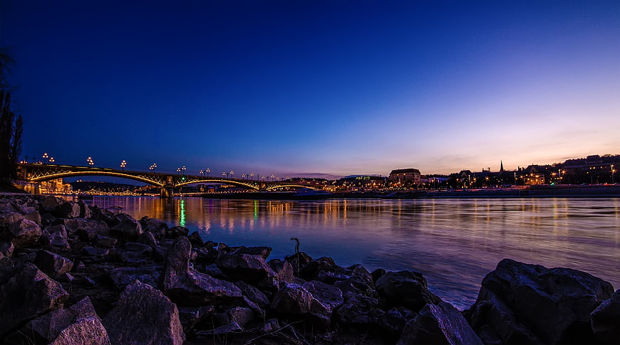 Illuminated Bridge Over River at Twilight with Rocky Foreground