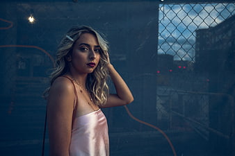 Stylish Blonde Woman in Pink Dress Against Urban Fence