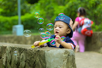 Toddler Boy Blowing Colorful Bubbles in Park