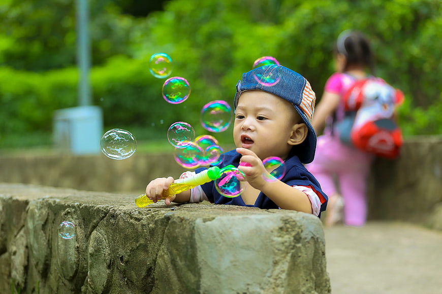 Toddler Boy Blowing Colorful Bubbles in Park
