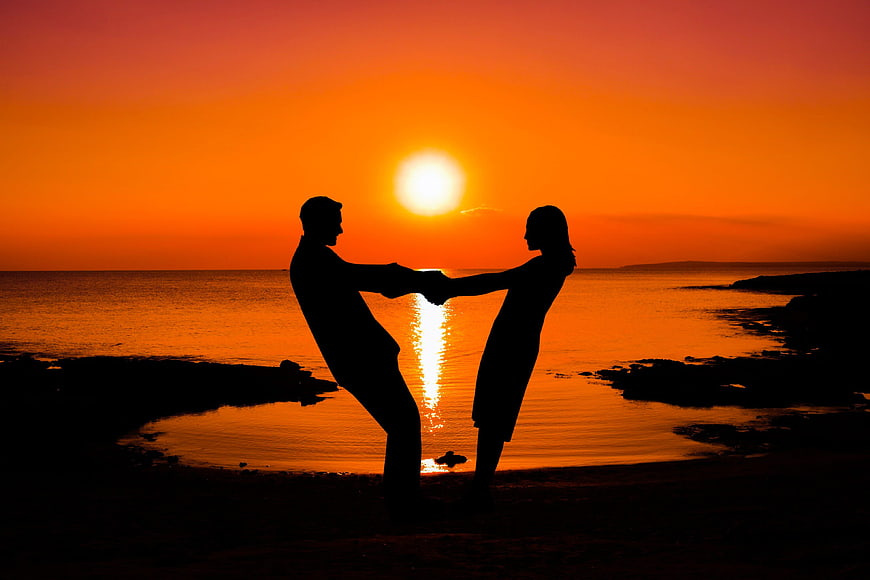 Silhouette of Romantic Couple Holding Hands at Sunset on Beach