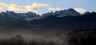Misty Mountain Panorama with Snow-Capped Peaks and Autumn Forest