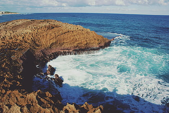 Aerial view of rugged coastal cliffs meeting turquoise ocean waves