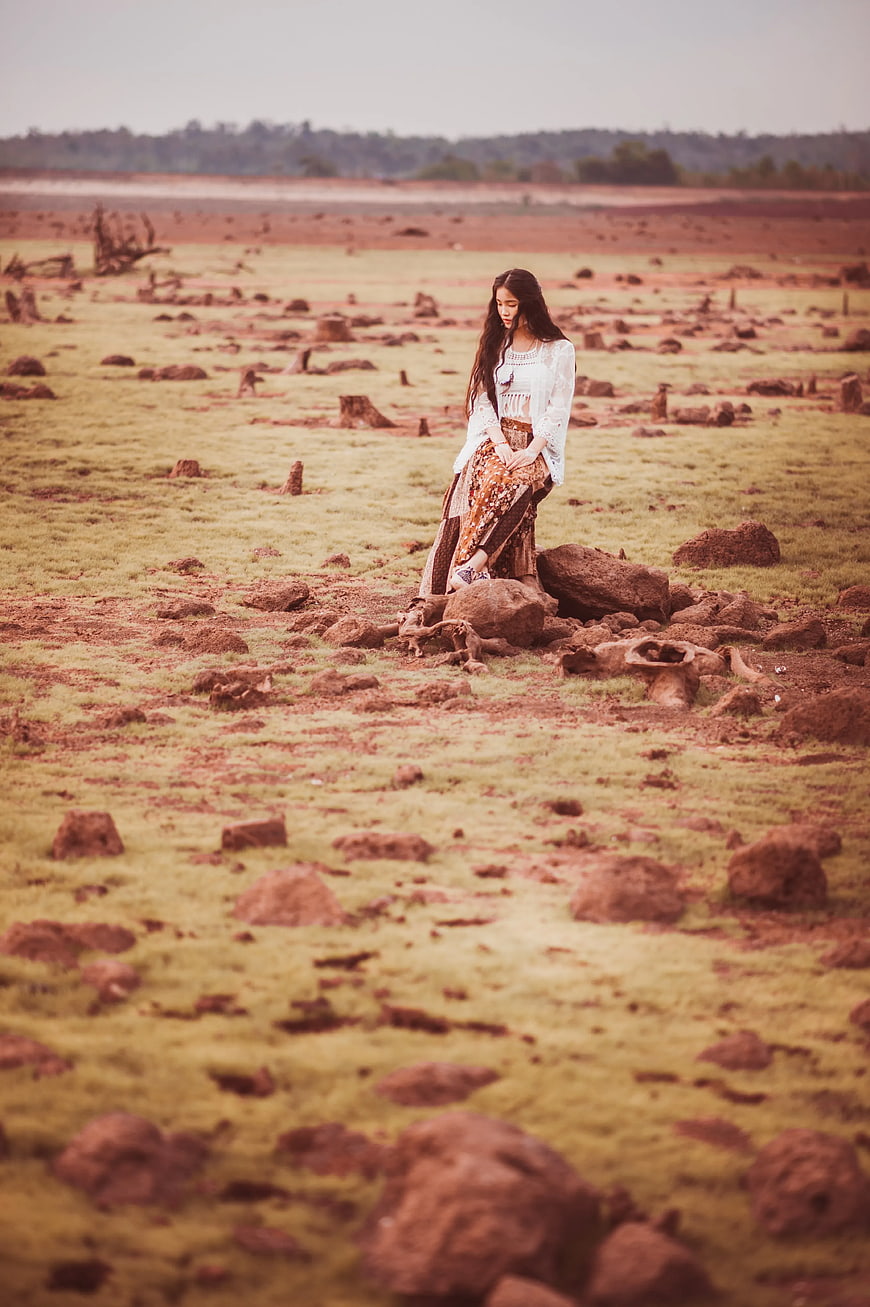 Woman in White Cardigan Sitting on Rock in Barren Landscape