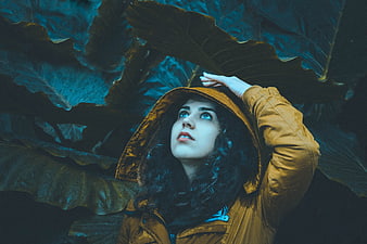 Woman in Yellow Raincoat Looking Up at Giant Leaves