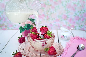 Pouring milk over fresh strawberries in a glass bowl