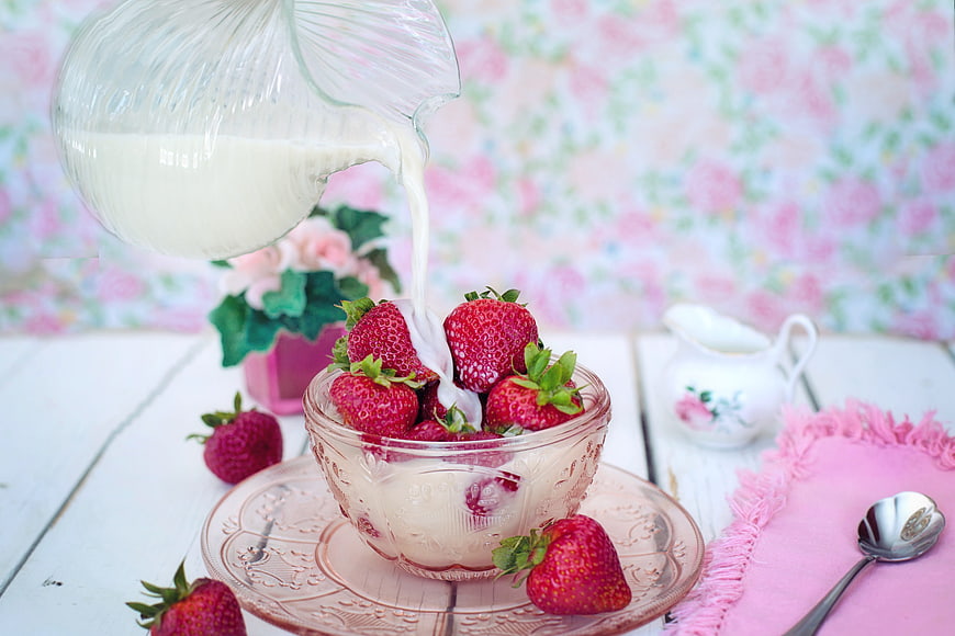 Pouring milk over fresh strawberries in a glass bowl