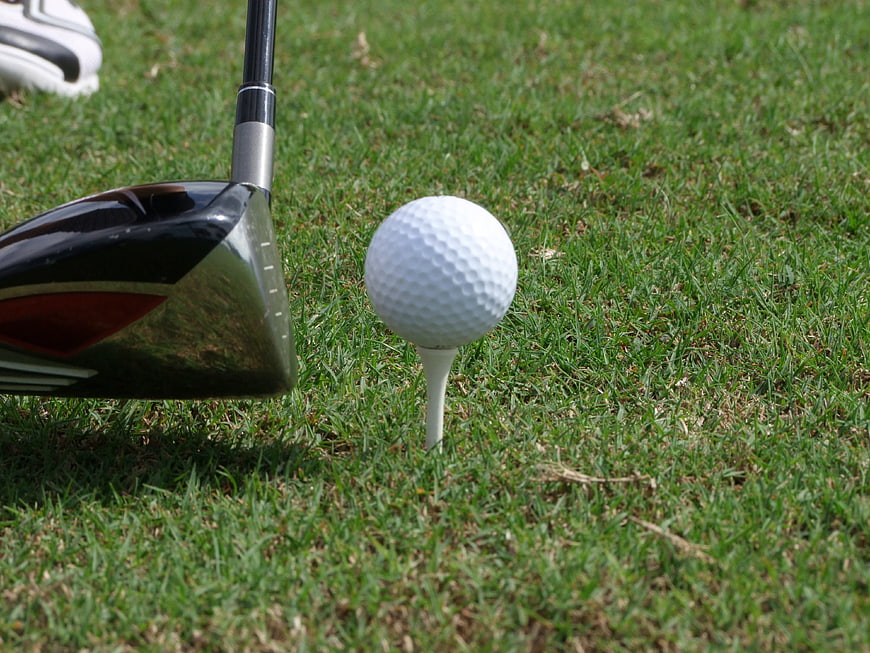 Golf ball on tee with driver club on green grass