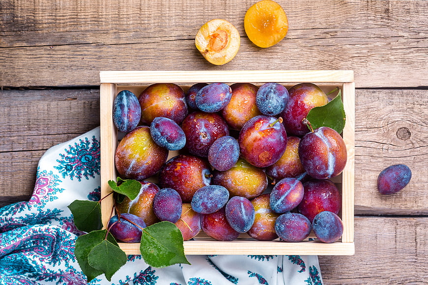 Fresh Summer Plums In Wooden Crate On Rustic Wood Table