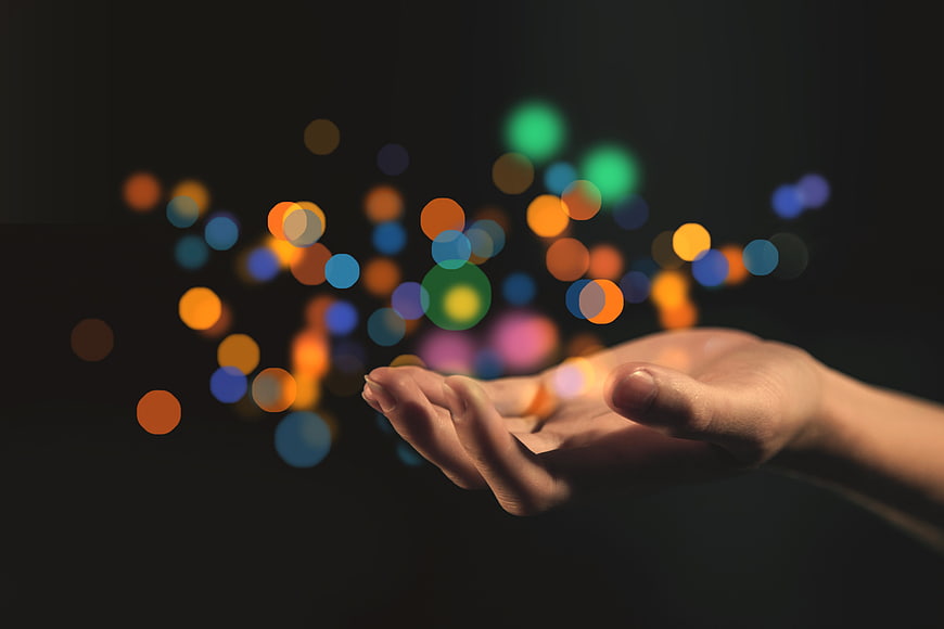 Open Hand Releasing Colorful Bokeh Lights Against Dark Background
