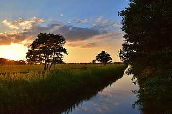 Serene River Sunset with Golden Sunbeams and Green Fields