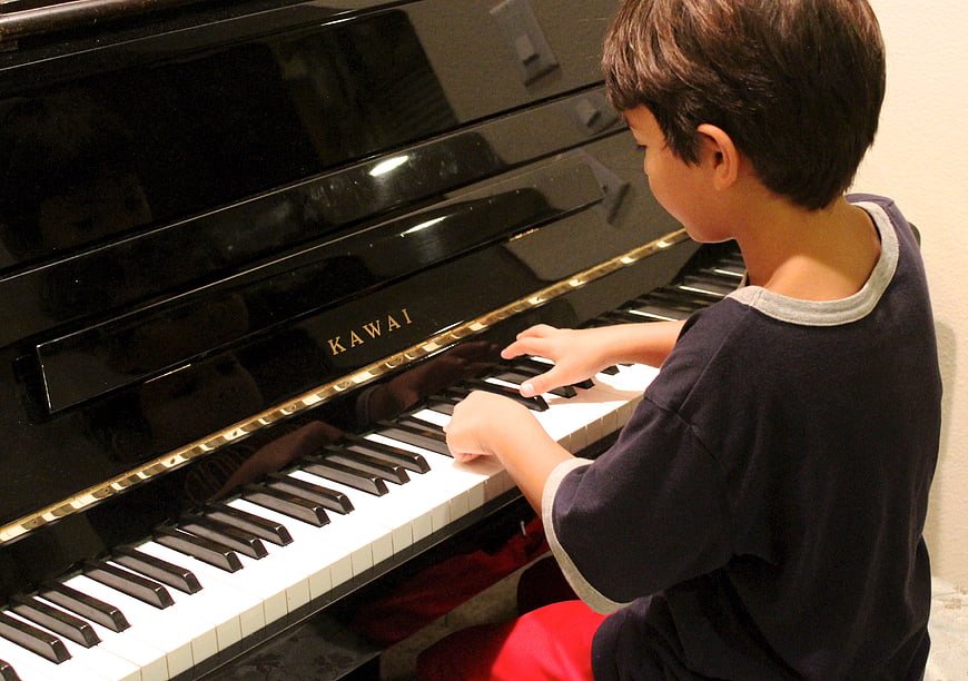 Young boy practicing on a black Kawai upright piano