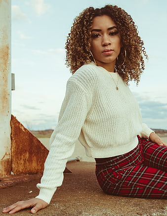 Stylish woman with curly hair sitting outdoors in plaid pants