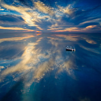Lone Boat on Calm Water with Dramatic Sunset Sky Reflection