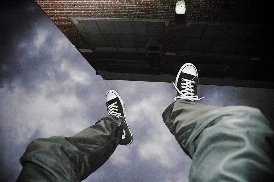 Upside down view of sneakers dangling over brick building edge