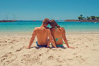 Young couple sitting on a sunny beach with turquoise ocean view