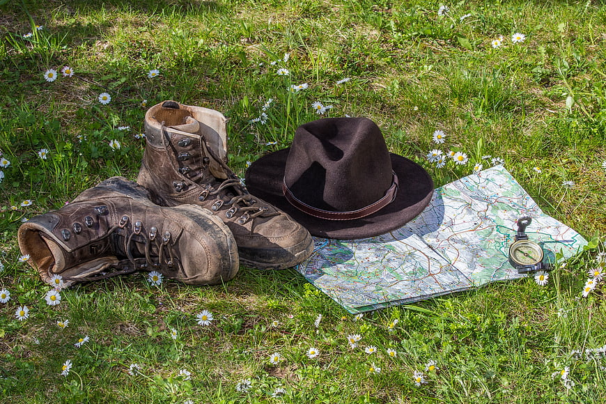 Vintage hiking boots, hat, map, and compass on grass