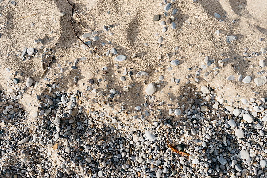 Top view of sandy beach with scattered pebbles and stones