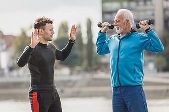 Senior man lifting dumbbells with personal trainer outdoors