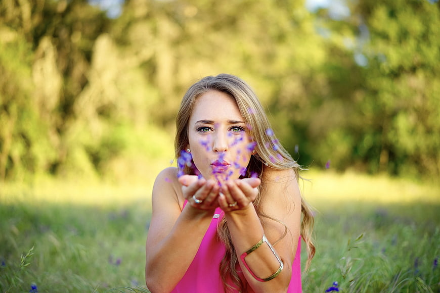 Woman Blowing Purple Petals in Green Meadow