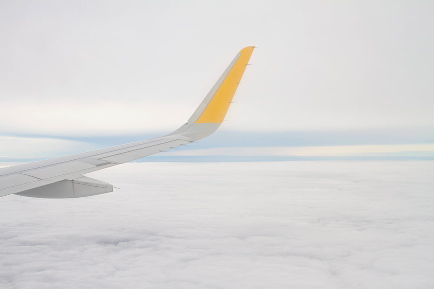 Airplane Wing Over Clouds with Yellow Winglet