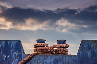 Rusty rope on blue ship bollard against dramatic stormy sky