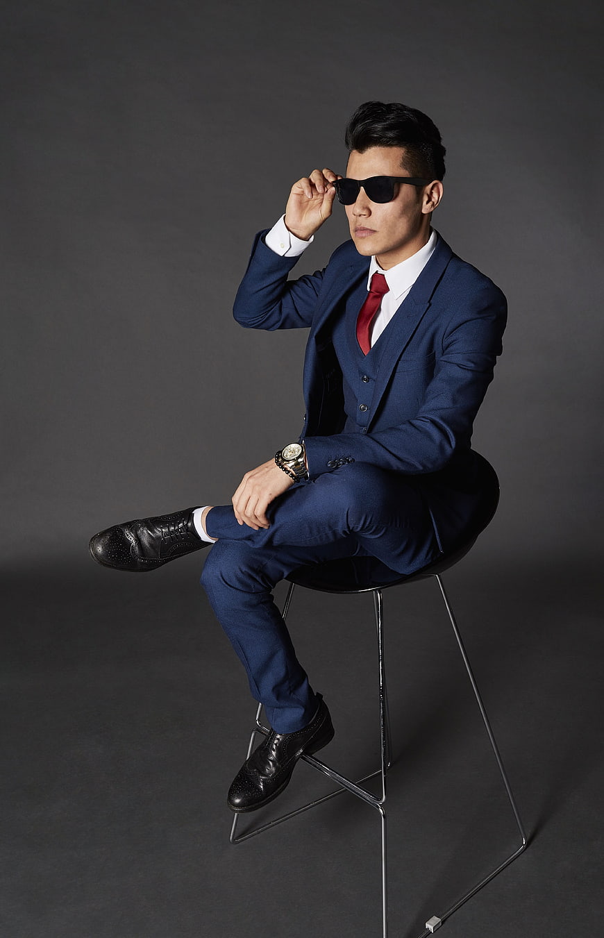 Confident Asian businessman in blue suit and sunglasses sitting on stool