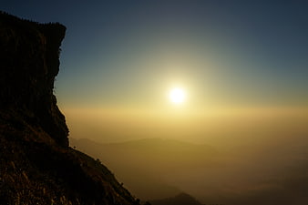 Sunset over misty mountain range with cliff silhouette