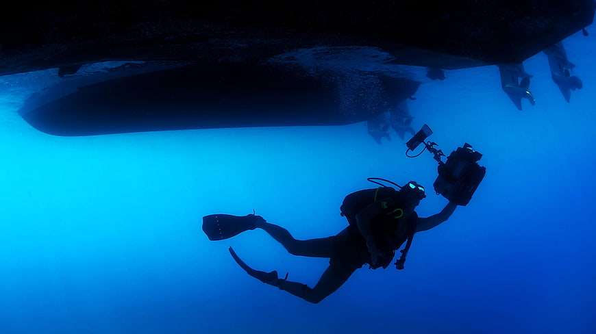 Underwater diver filming boat hull with camera
