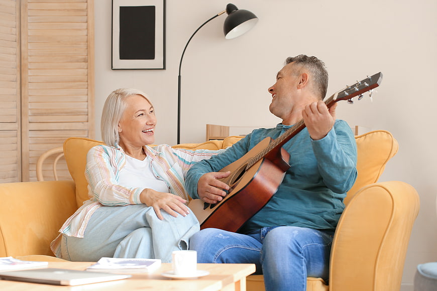 Happy Senior Couple Playing Guitar on Sofa at Home