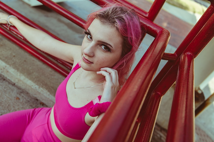 Young woman with pink hair in athletic wear on red stairs
