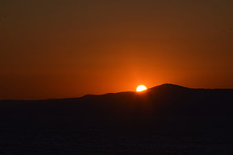 Silhouette of mountain range against vibrant orange sunset sky