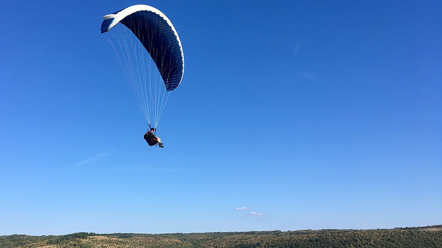 Paraglider soaring high against a clear blue sky
