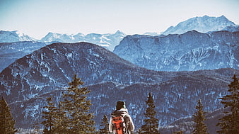 Hiker with backpack looking at snowy mountain peaks