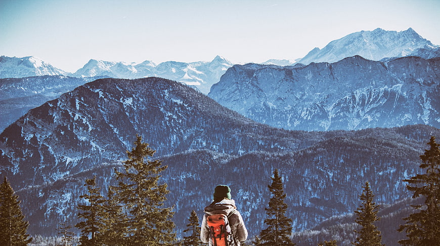 Hiker with backpack looking at snowy mountain peaks